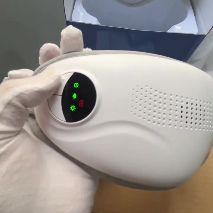 Gloved hand pressing the power button on a Nexora heated eye massager, screen lit